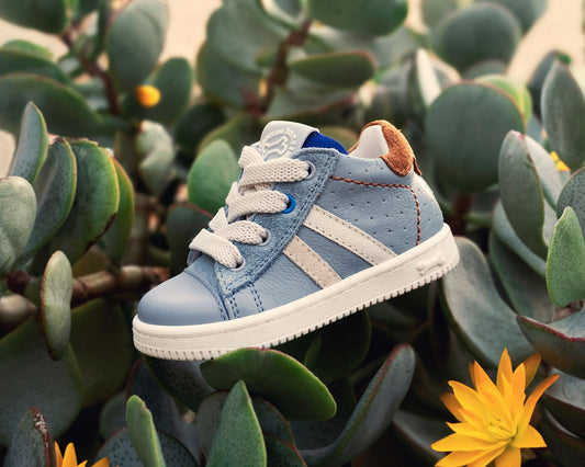 A baby shoe is surrounded by leafy green plants.